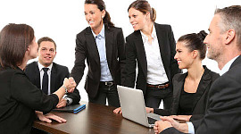 women shaking hands at a business meeting, with men loooking on