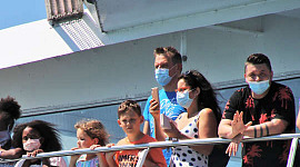 people, most wearing masks, standing on the railing of a cruise ship